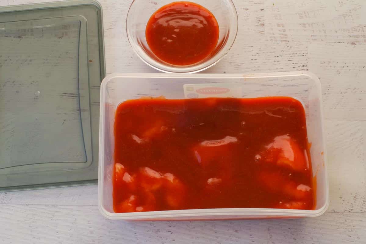 Chicken covered in marinade in plastic container.