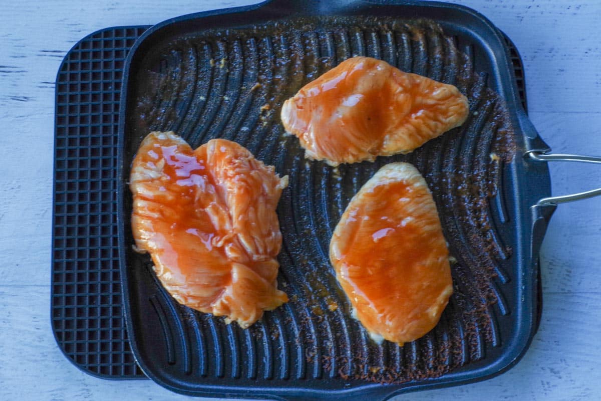 Raw marinated chicken on stovetop grill.