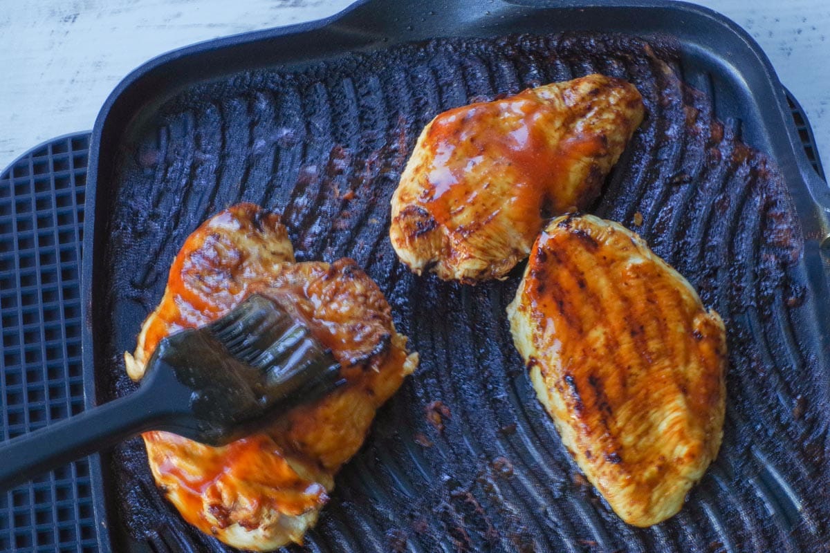 Cooked monterey chicken breast being basted with additional marinade on indoor stovetop grill.
