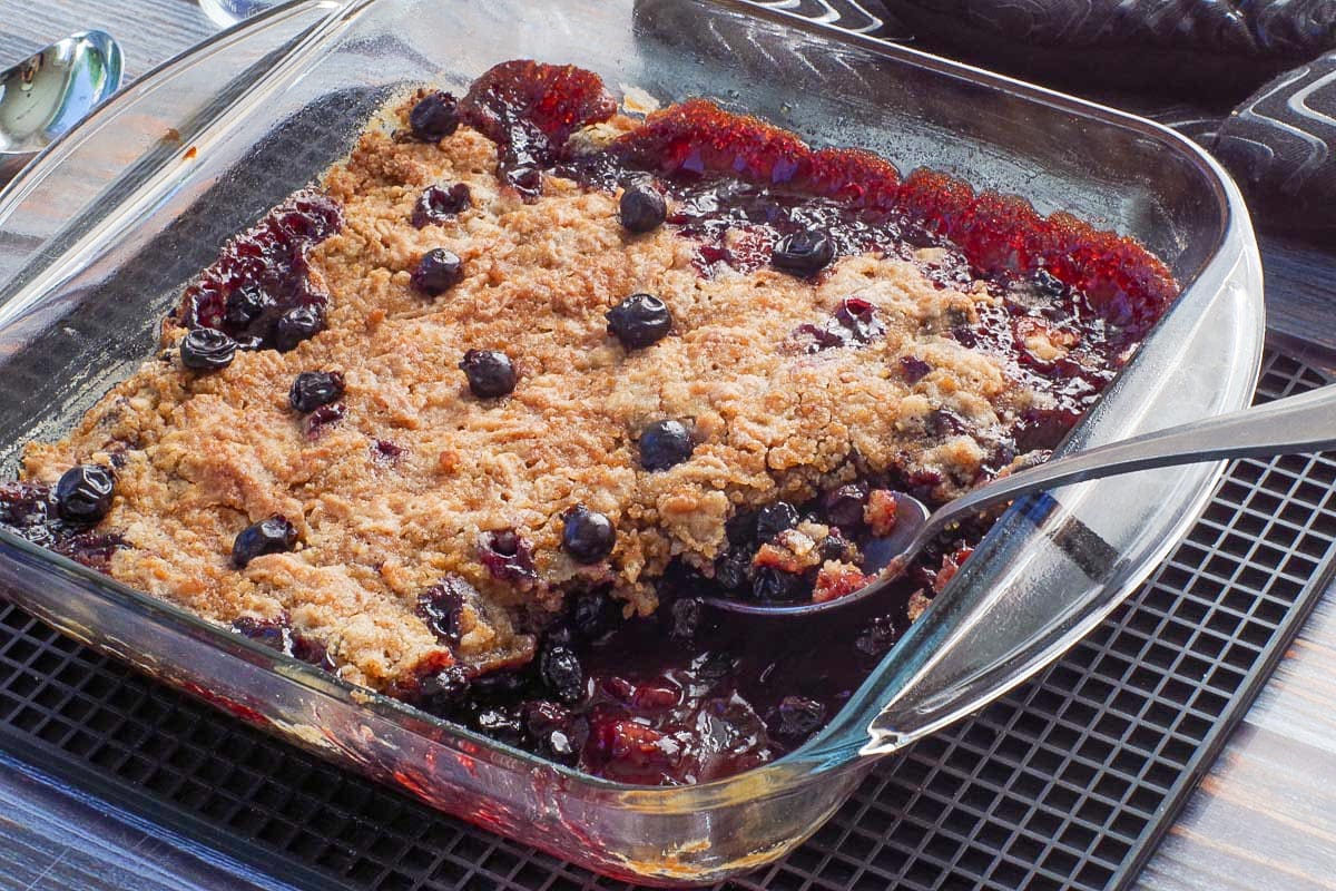 Saskatoon berry Crumble in a square glass pan with some crumble missing and a spoon in the pan.