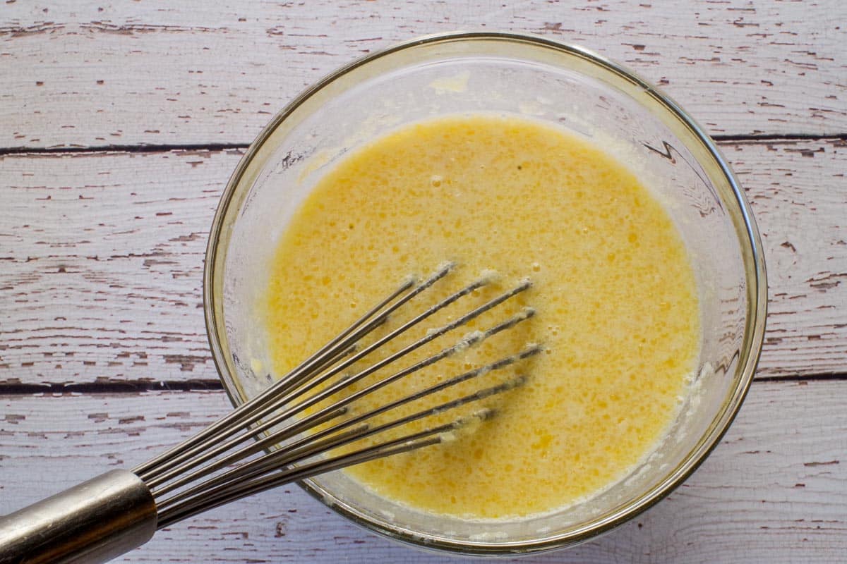 Wet ingredients whisked together in a glass bowl with a metal whisk.