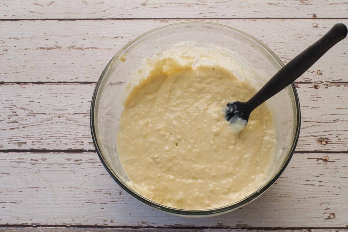 Wet and dry ingredients mixed together in a glass bowl with a black spatula.