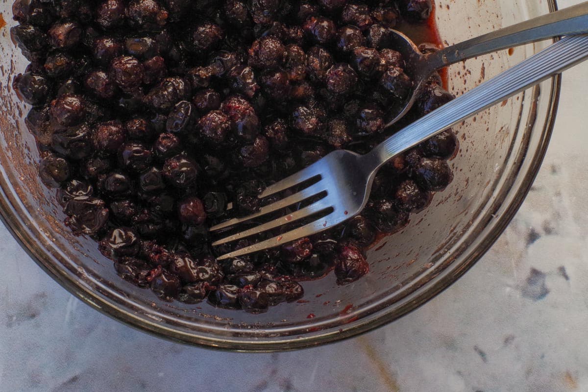 A fork mashing some of the Saskatoon berries in a medium glass bowl.