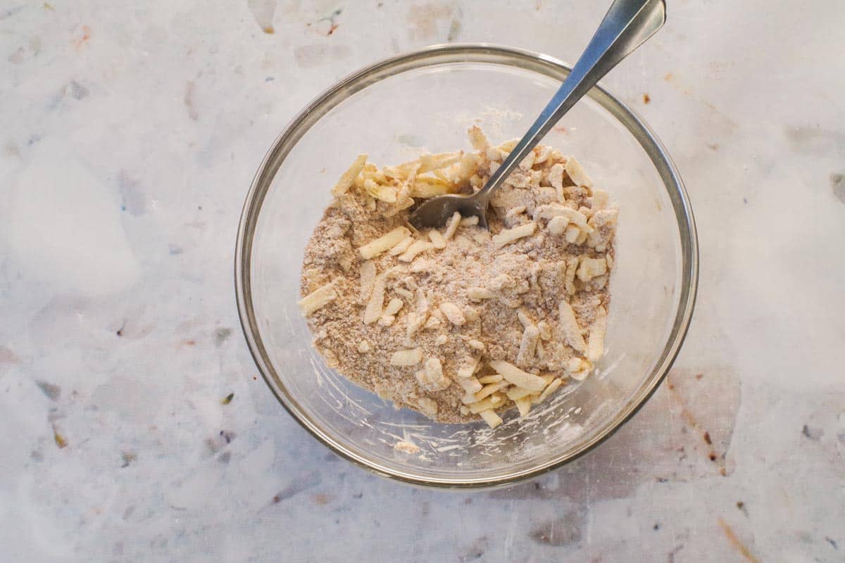 Grated butter mixed in with dry ingredients in a medium glass bowl.