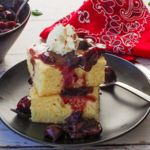 Fresh Cherry Sauce poured over 2 stacked oven baked pancakes with more cherry sauce in the background.