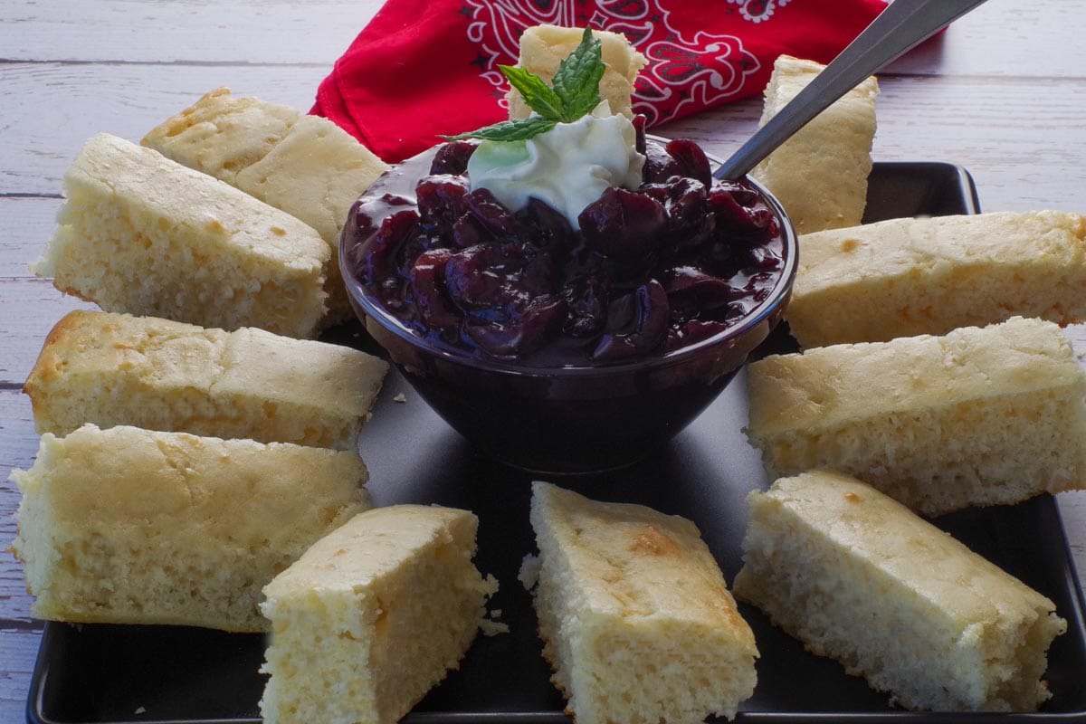 Oven baked pancakes cut into dippers on a black try with cherry sauce in the middle in a galss bowl