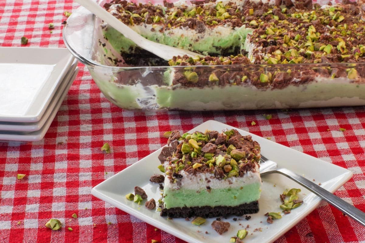 A piece of Pistachio Ice Cream Dessert on a white square plate, with more pistachio ice cream dessert in the background.