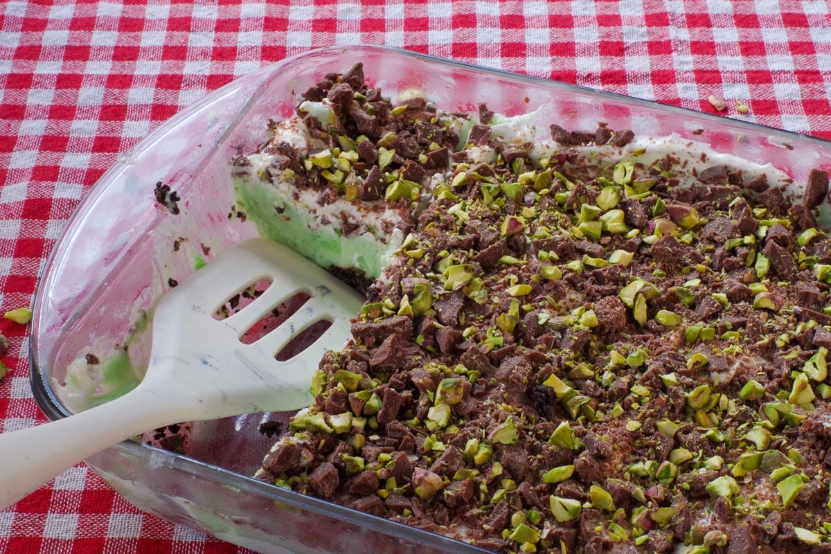 Pistachio Ice Cream Dessert in a 9x13 glass poan with 2 pieces missing and a spatula in that space in the pan.