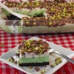 A piece of Pistachio Ice Cream Dessert on a white square plate, with more pistachio ice cream dessert in the background.