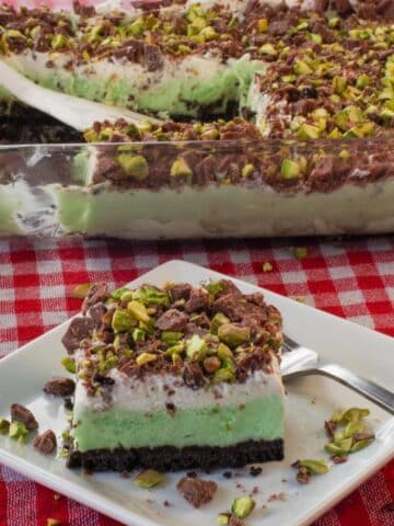 A piece of Pistachio Ice Cream Dessert on a white square plate, with more pistachio ice cream dessert in the background.