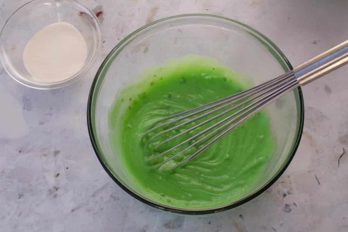 Pistachio pudding and milk mixed together in a large glass bowl with a whisk.