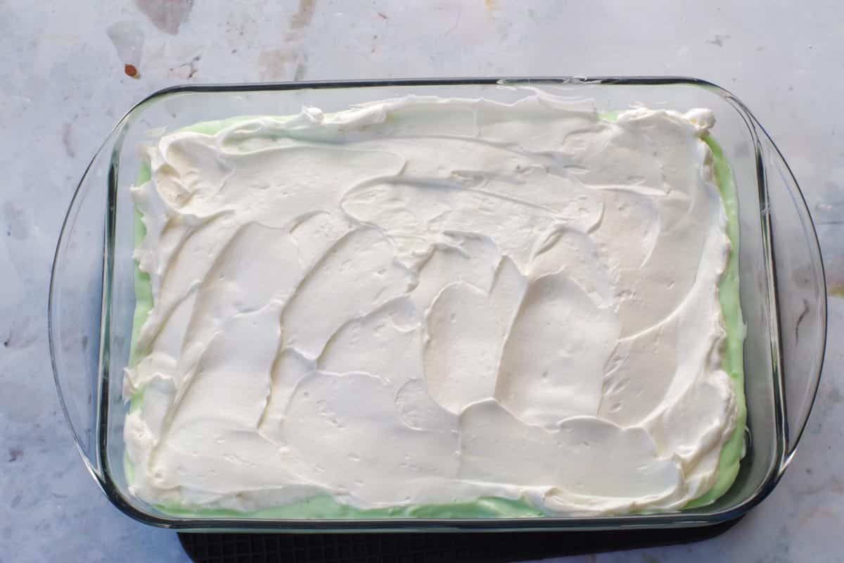 Whipped cream spread over pistachio ice cream layer in 9x13 glass pan.