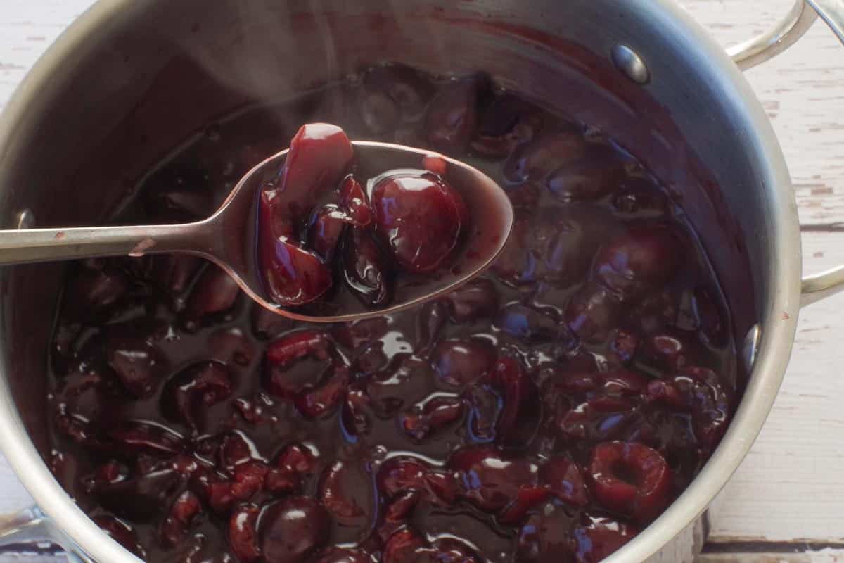 Healthy and Fresh Cherry Sauce on a spoon over a pot of more cherry sauce.