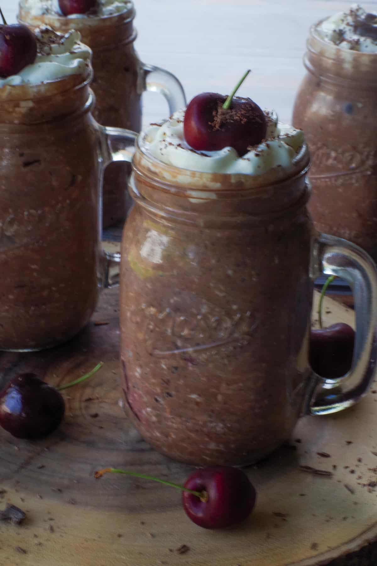 A jar of black forest overnight oats on a wooden stand , with 3 more in the background.