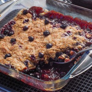 Saskatoon berry Crumble in a square glass pan with some crumble missing and a spoon in the pan.