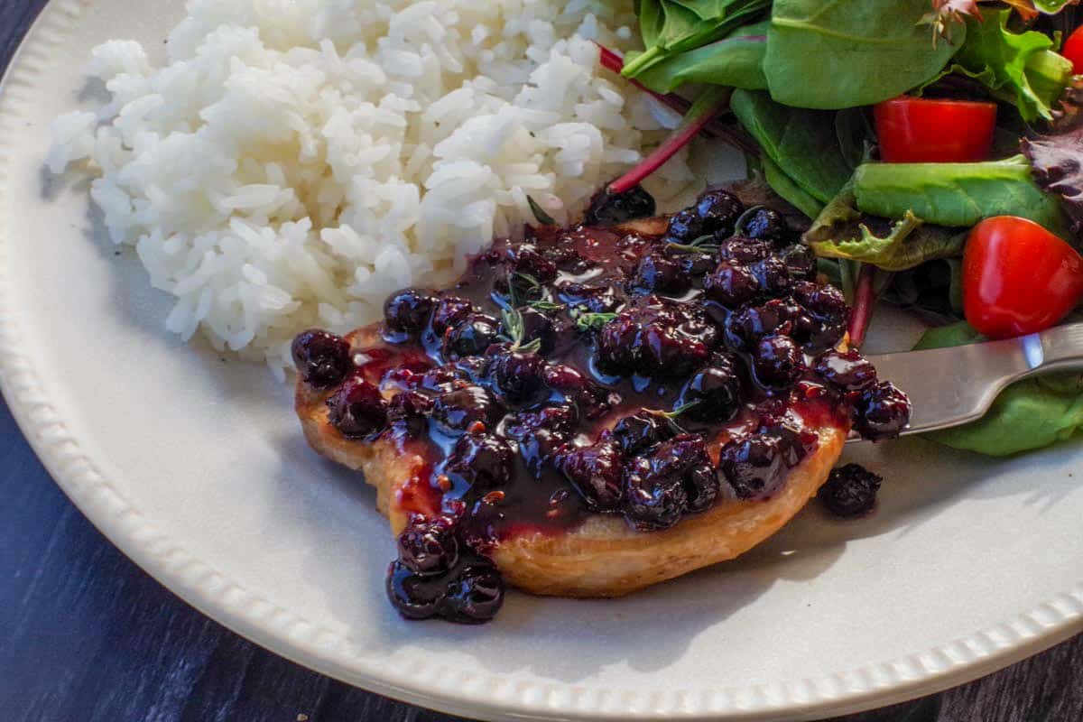 Savory Saskatoon Berry Sauce on a piece of grilled pork with rice and salad on the plate.