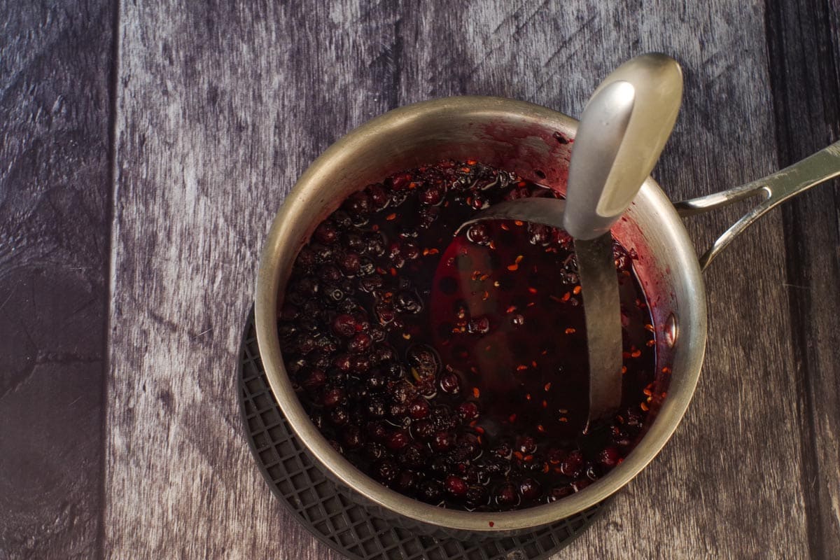Saskatoon berry mixture simmered in small saucepan, with half the berries mashed.