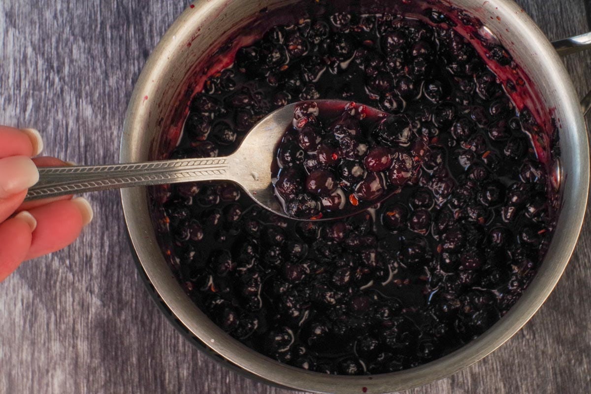 Saskatoon berry meat sauce on a spoon, over a saucepan with more sauce to show how thick it should be.