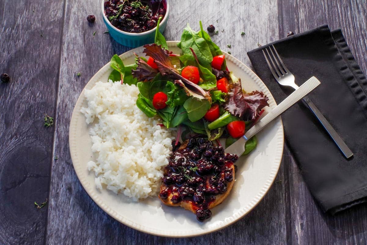 Savory Saskatoon Berry Sauce on a piece of grilled pork with rice and salad on the plate