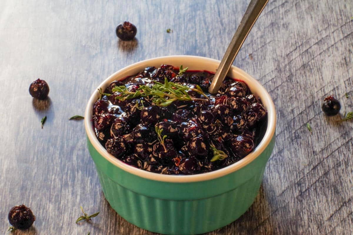 Savory Saskatoon Berry Sauce in a turquoise dish with a spoon.