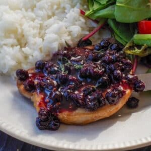 Savory Saskatoon Berry Sauce on a piece of grilled pork with rice and salad on the plate