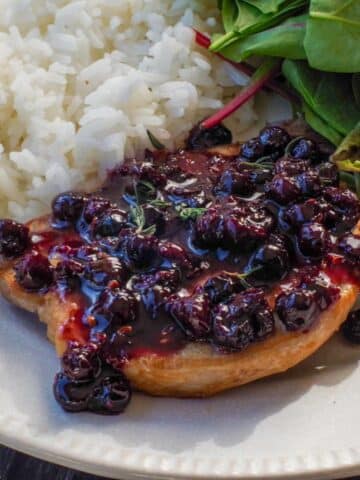Savory Saskatoon Berry Sauce on a piece of grilled pork with rice and salad on the plate