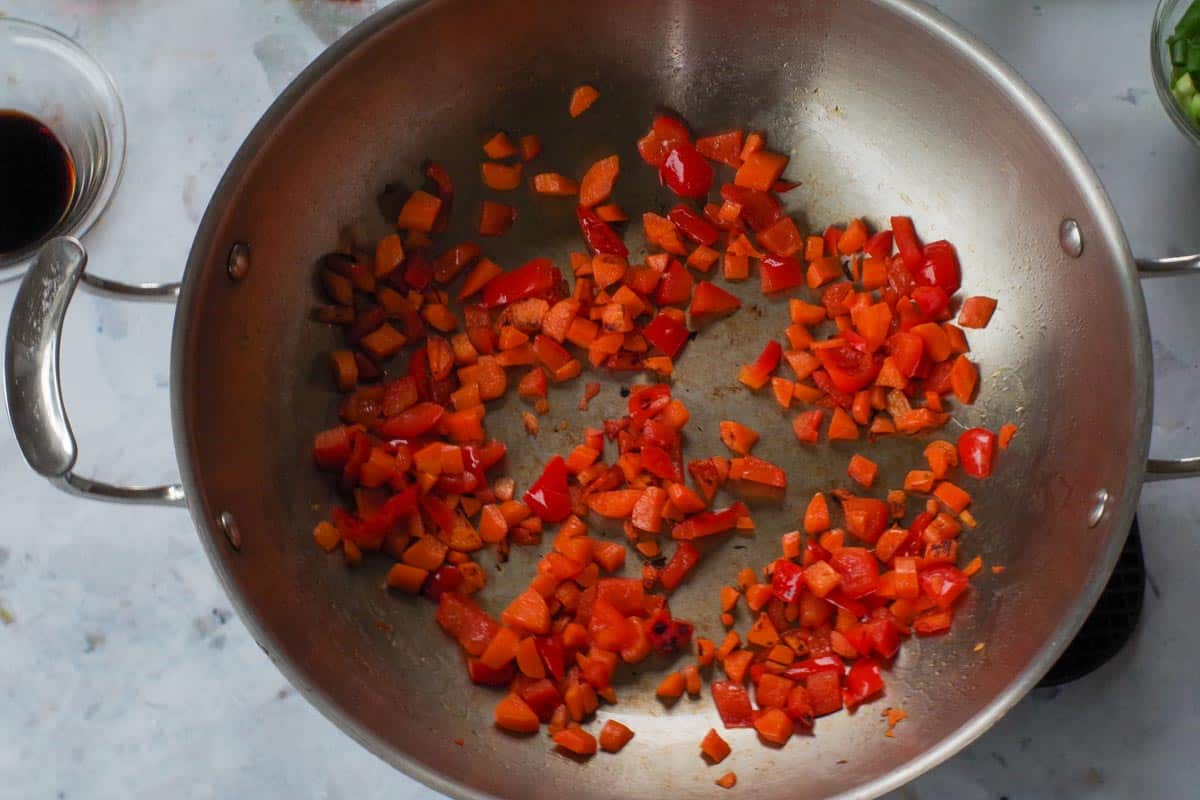 Carrot and red pepper being cooked in oil in wok.