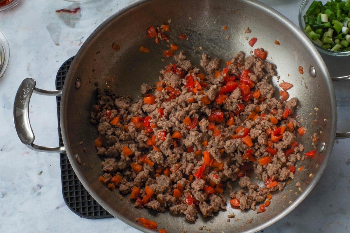 Ground chicken cooked with carrot and red pepper mixture in wok.