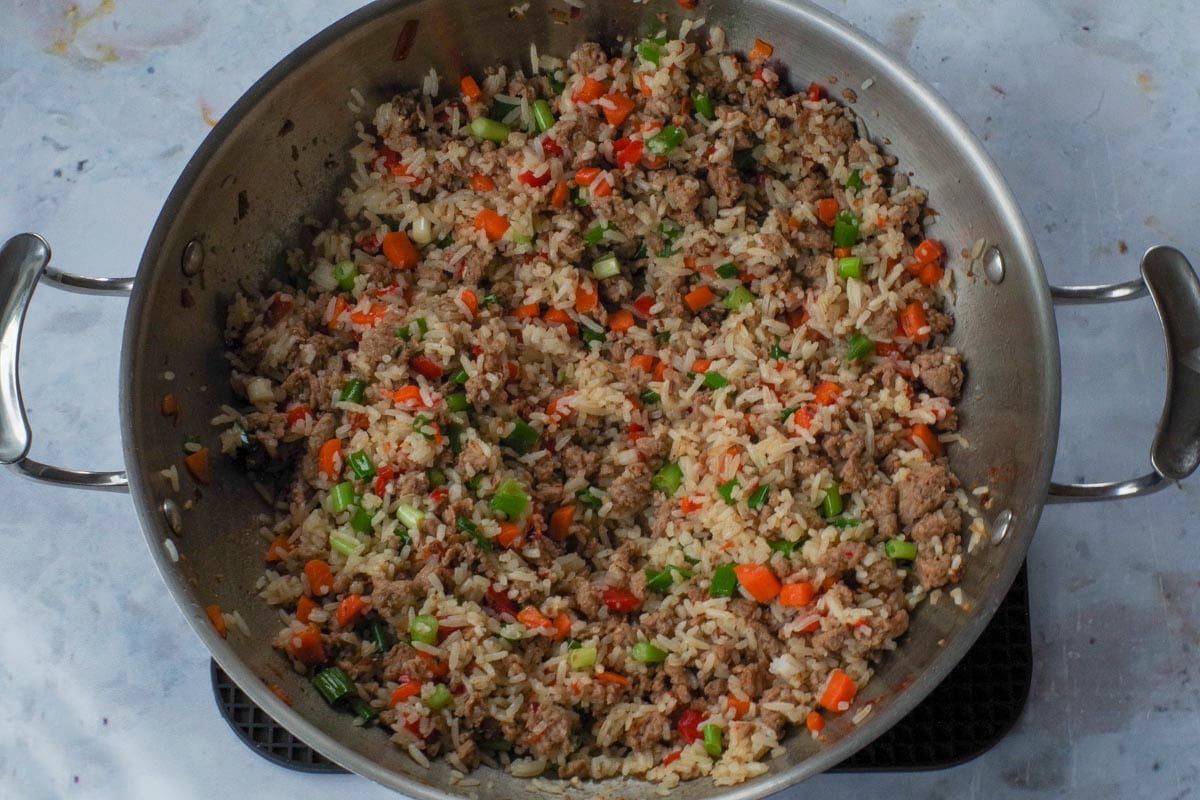 Rice and green onion added to chicken and veggie mixture in wok.
