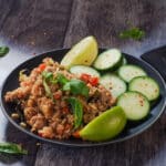 Thai Basil Fried Rice (with chicken), cucumbers and lime wedges on a black plate
