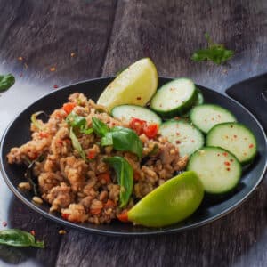 Thai Basil Fried Rice (with chicken), cucumbers and lime wedges on a black plate
