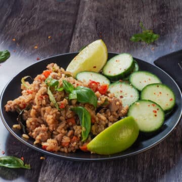 Thai Basil Fried Rice (with chicken), cucumbers and lime wedges on a black plate