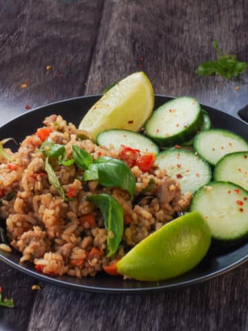 Thai Basil Fried Rice (with chicken), cucumbers and lime wedges on a black plate