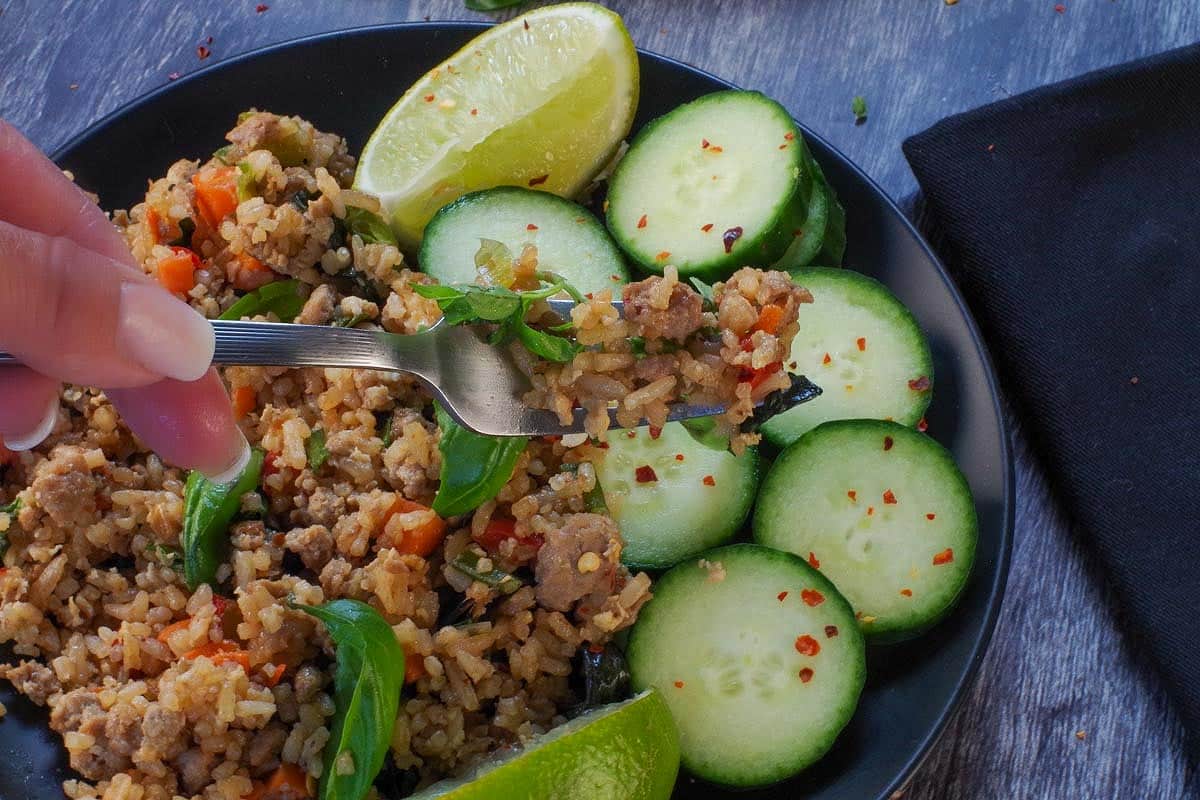 Thai basil fried rice being held up on a fork over a plate of more fried rice with cucumbers.