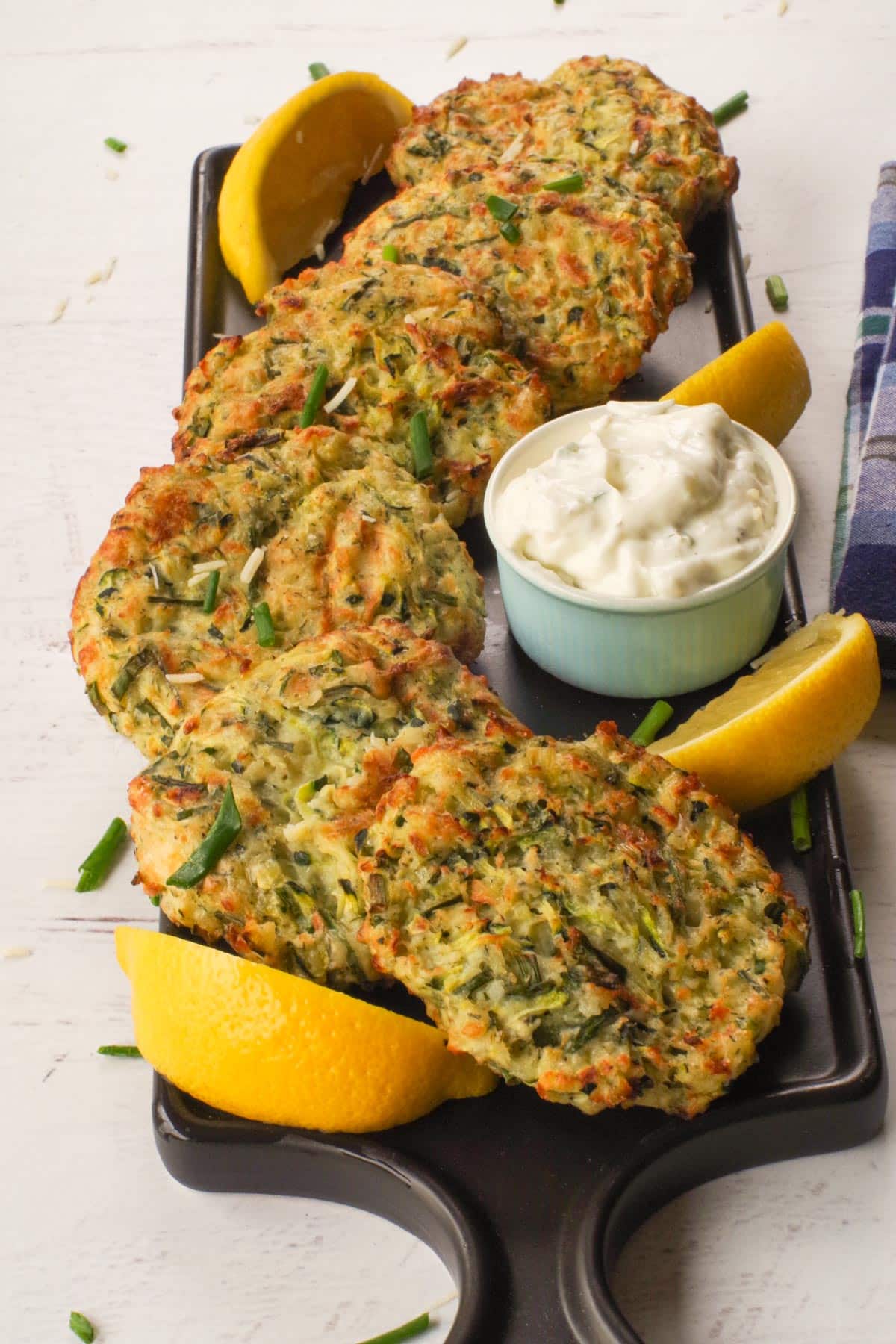Air fryer zucchini patties slightly overlapping in an S shape on a black tray with lemon and tzatziki.