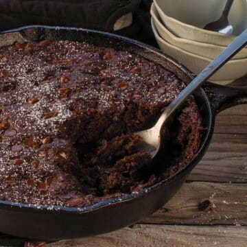 Chocolate Zucchini Spoon Cake in a cast iron pan with cake missing and a spoon in that space.