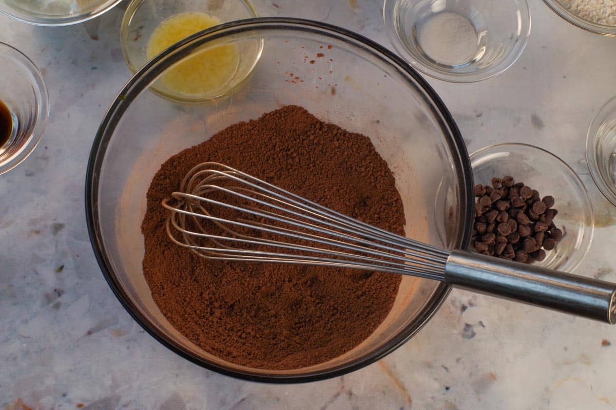 Brown sugar and unsweetened cocoa for Chocolate Zuchinni Spoon Cake stirred together with large metal whisk in large glass bowl.