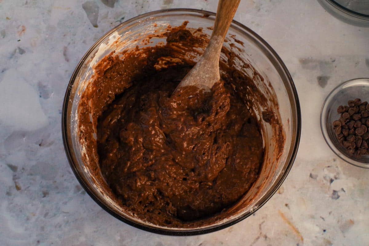Dry ingredients gently folded into the wet ingredients with wooden spoon in a large glass bowl.
