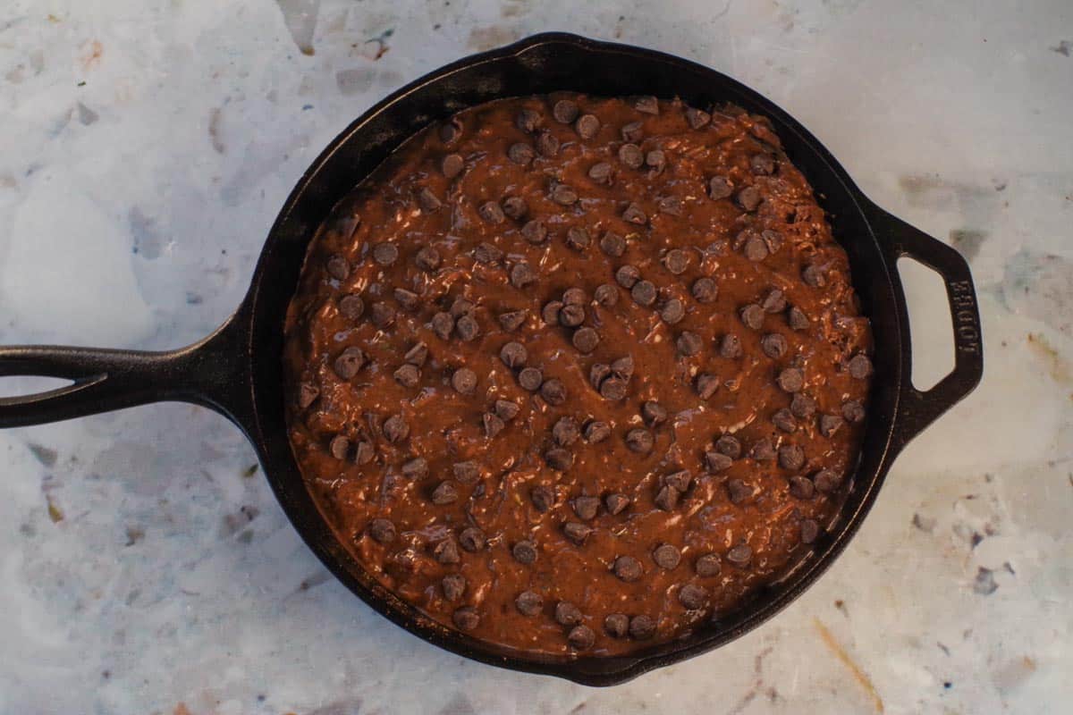 Chocolate chips sprinkled over the zucchini spoon cake batter in cast iron frying pan.