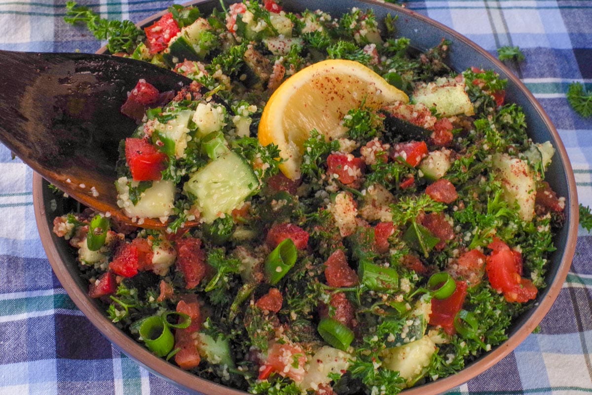 A bowl of Mediterranean Tabouli salad with a a dark wooden spoon scooping out some salad.