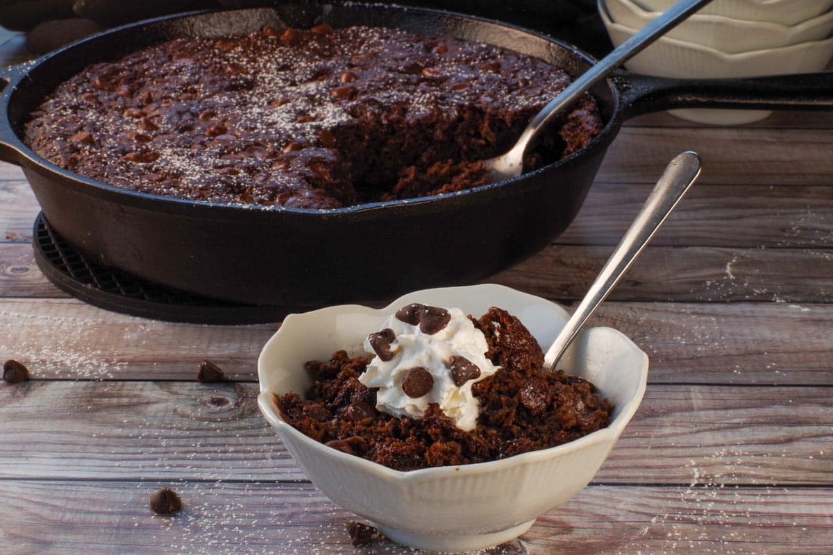 Easy Chocolate Zucchini Spoon Cake in a small white flour blow with more cake in the cast iron skillet in the background.