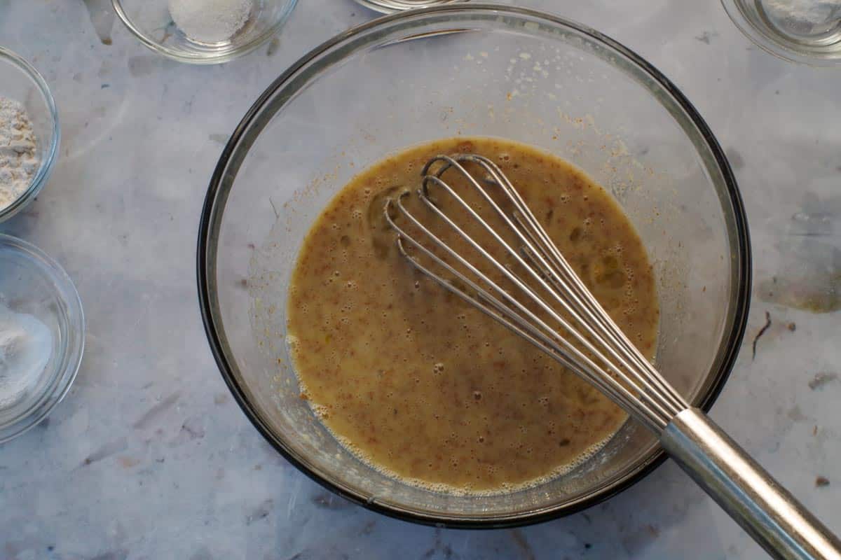 Wet ingredients in Healthy Saskatoon Berry Oatmeal Bars in a large glass bowl being stirred with a whisk.