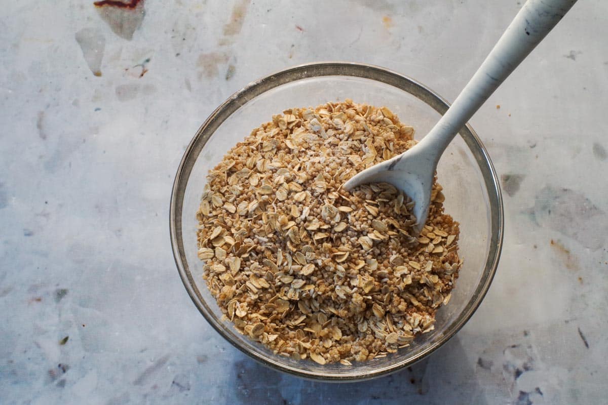 Dry ingredients in Healthy Saskatoon Berry Oatmeal Bars in a medium glass bowl, being stirred with a silicone spoon.