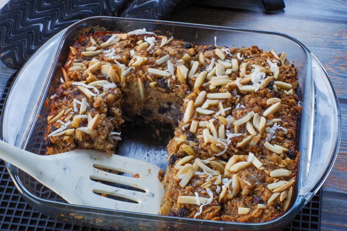 Healthy Sasktoon Berry Oatmeal Bars in an 8x8 glass pan with several pieces missing and a white spatula in the pan.