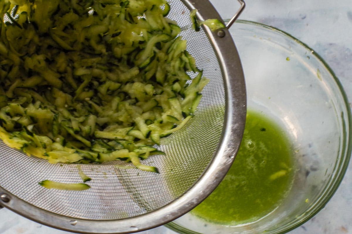 Grated zucchini pushed through a sieve, with liquid in glass bowl below.