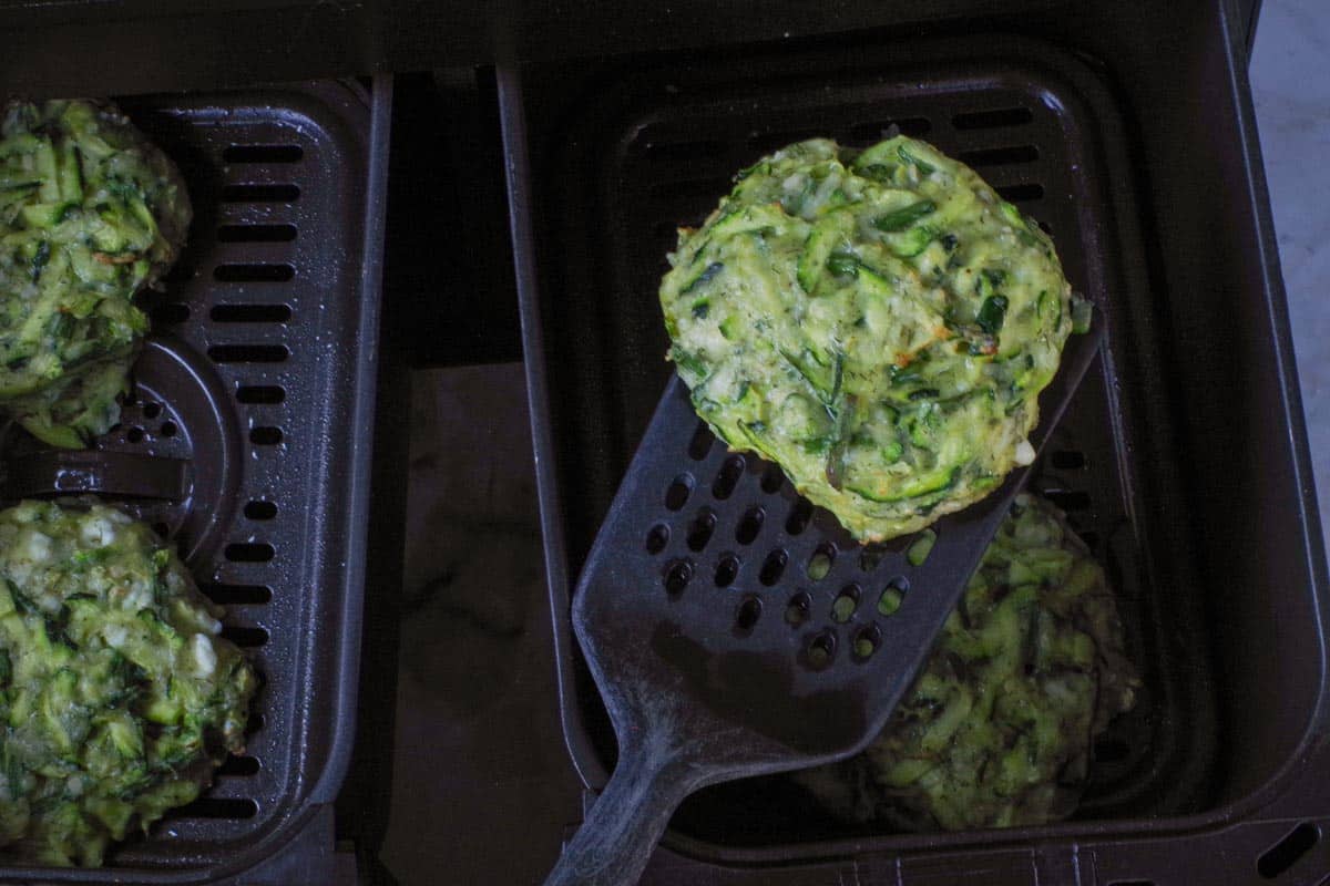 Zucchini fritter air fried for 7 minutes, being held up with a spatula.