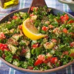 A bowl of Mediterranean Tabouleh Salad with a dark wooden spoon in it, on a blue and white checked table cloth.