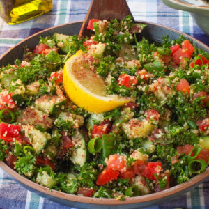 A bowl of Mediterranean Tabouleh Salad with a dark wooden spoon in it, on a blue and white checked table cloth.