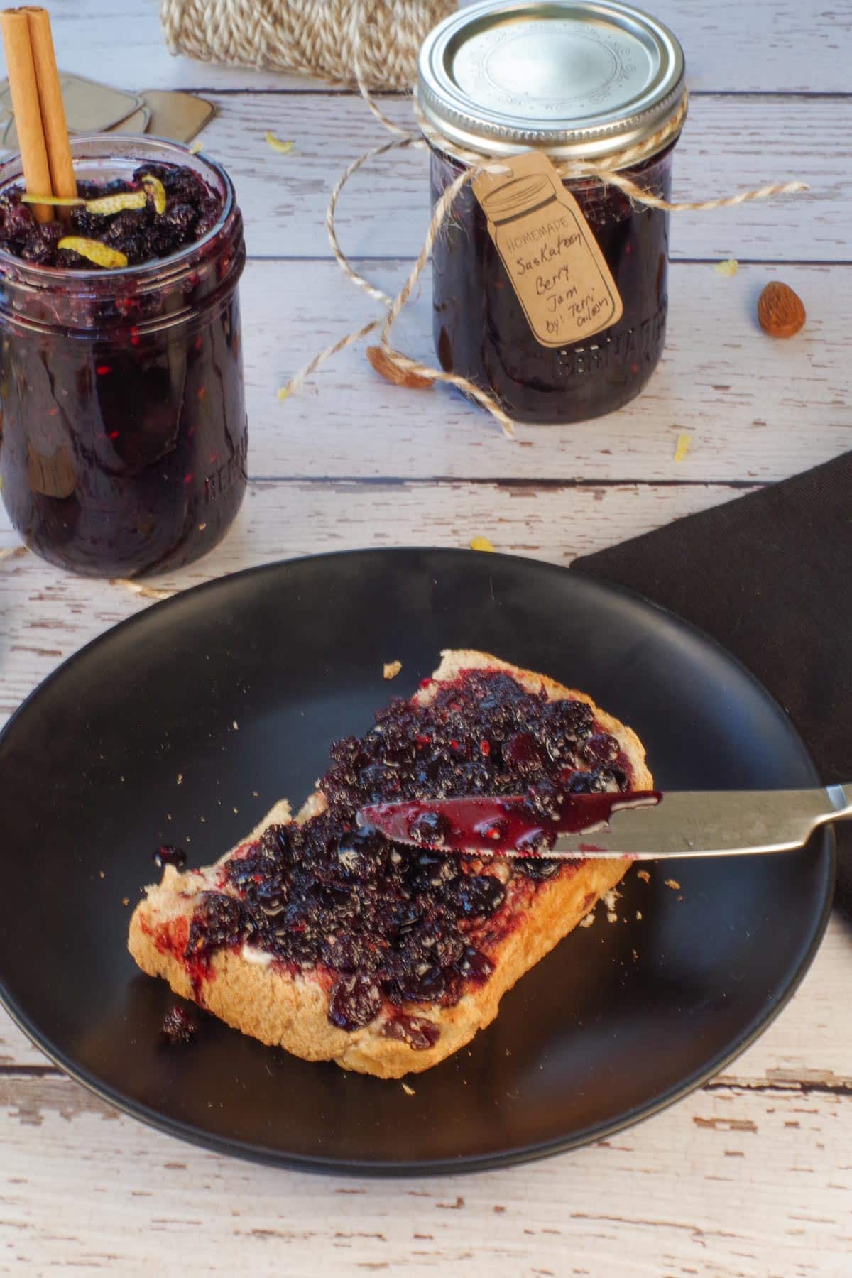 Saskatoon berry jam on raisin toast with 2 jars of jam in the background.
