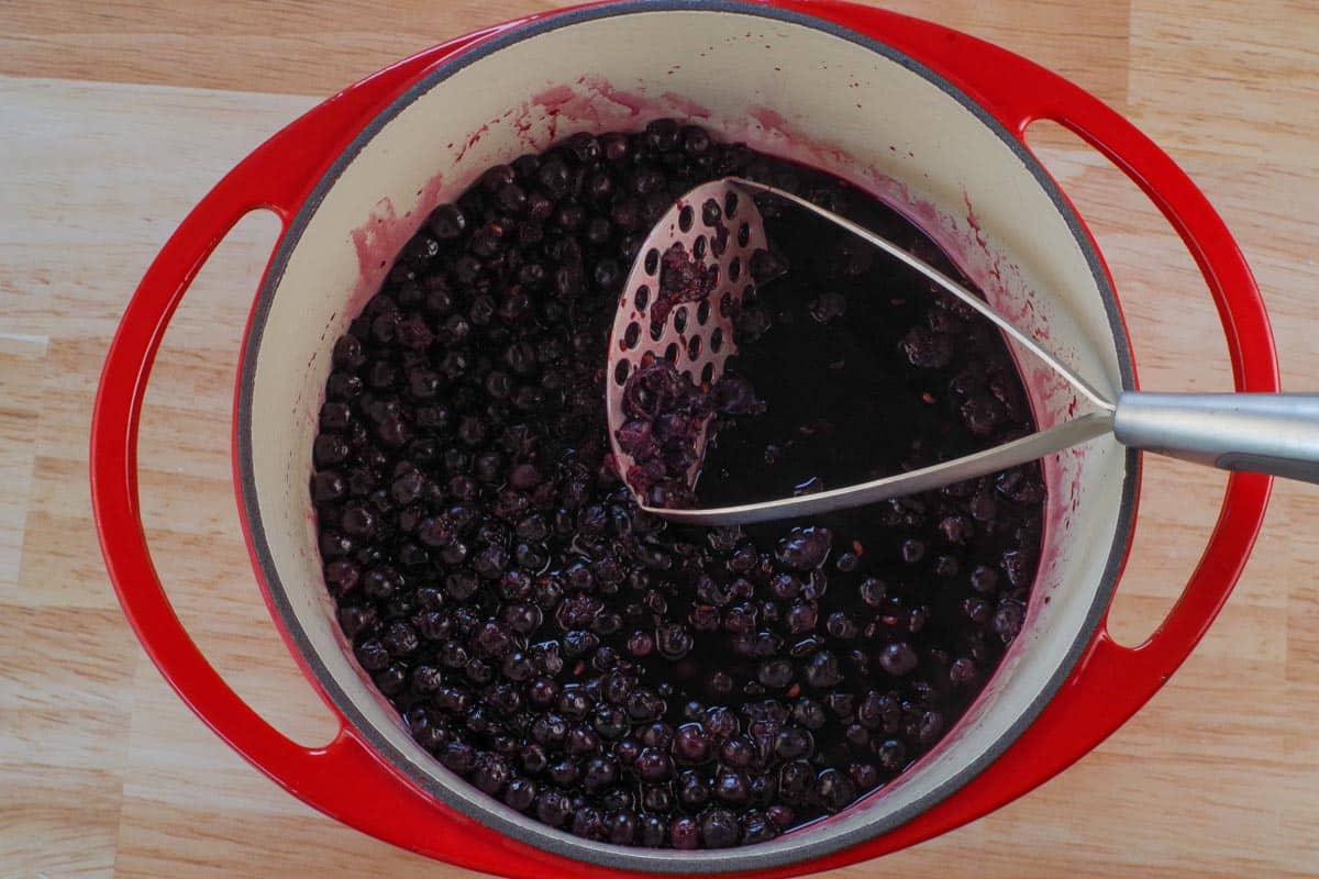 Saskatoon Berries in Dutch oven being mashed (25%) with a potato masher.